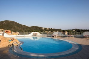 Una piscina con valla perimetral, sillas de descanso y montañas al fondo.