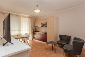 A modern kitchen with a dining area, a flat-screen TV, and two armchairs.