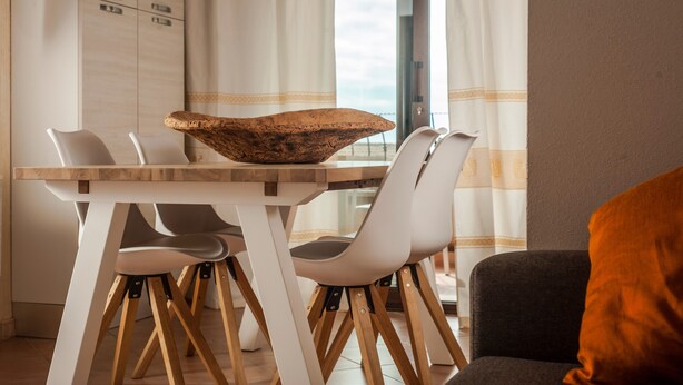 Un comedor con una mesa de madera, sillas blancas y un cuenco grande tejido.