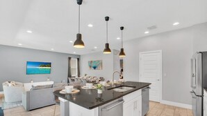 A modern kitchen with a central island, stainless steel appliances, pendant lighting, and a dining area with a sofa and table. - Your Own Tropical Oasis! 6 mi to Disney! (Kissimmee)