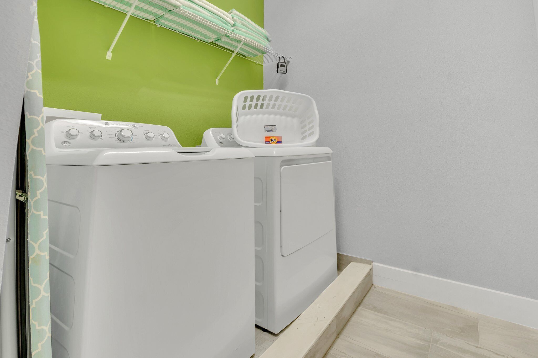 Zona de bugaderia amb rentadora i assecadora, una cistella i una paret verda.
