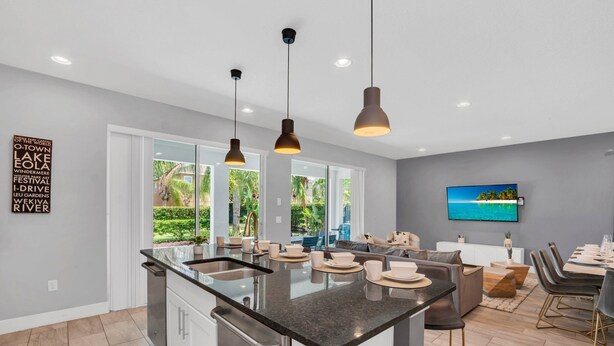 A modern kitchen with a central island, pendant lighting, and a dining area with a view of the outdoors. - Your Own Tropical Oasis! 6 mi to Disney! (Kissimmee)