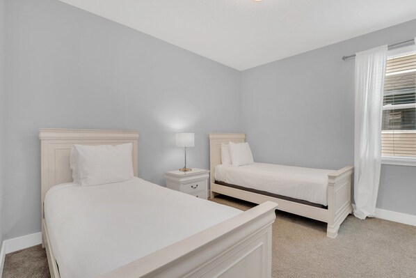 Een slaapkamer met twee eenpersoonsbedden, een nachtkastje met een lamp en een raam met gordijnen.