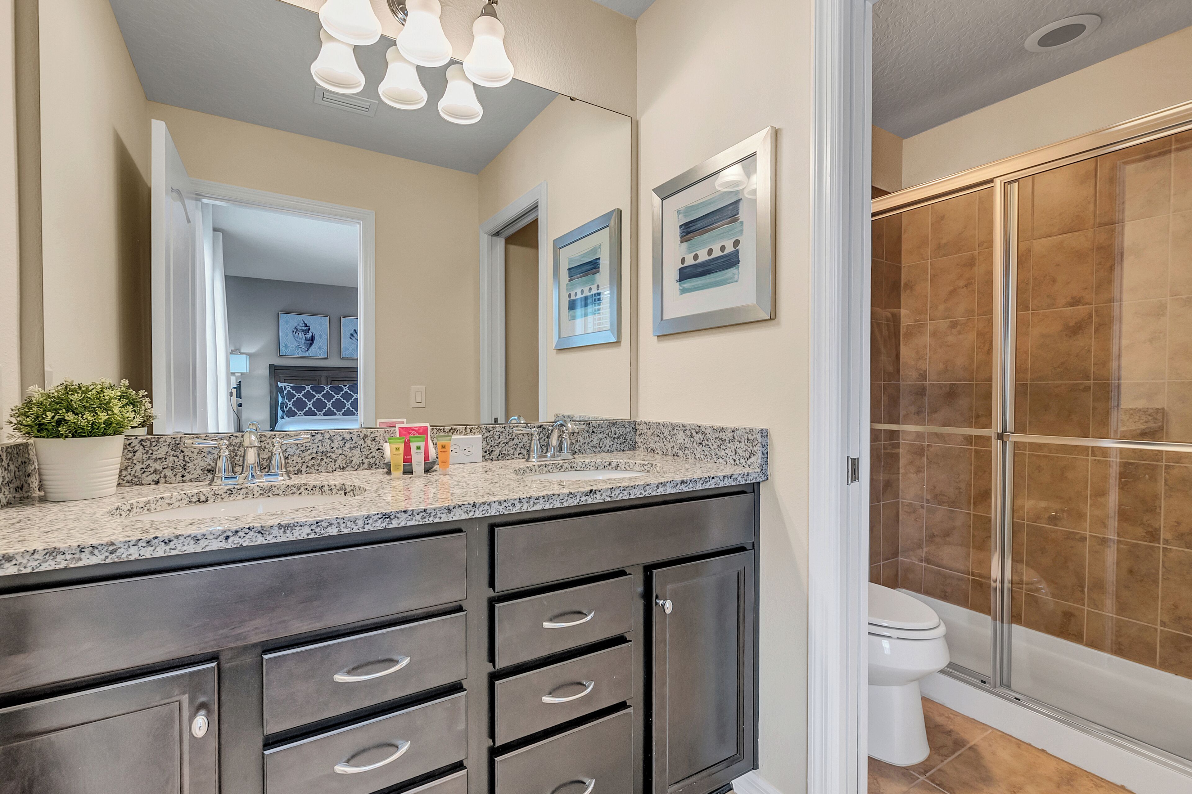A bathroom with a granite countertop, dark cabinets, a shower enclosure, and a large mirror.