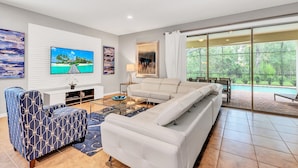 A modern living room with a large sectional sofa, a patterned armchair, a glass coffee table, and artwork on the walls. - Villa W/ Pool, Movie Theater & Game Roomsleeps 20 (Kissimmee)