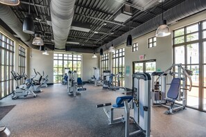 A spacious gym with various exercise machines, large windows, and a high ceiling with industrial-style lighting. - 4567 Narrative Lane (Kissimmee)