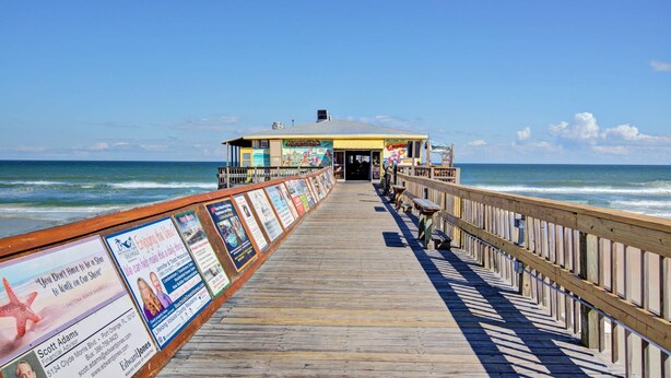 A wooden pier leading to a building with a signboard, surrounded by the ocean. - Oceanfront 1BR | Balcony | Steps to Sunglow Pier | Free Daily Activities Included (Daytona Beach Shores)