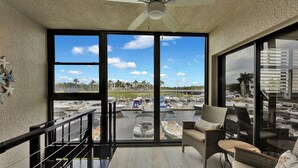 Un balcón con vista a un puerto deportivo, muebles de mimbre y un ventilador de techo.
