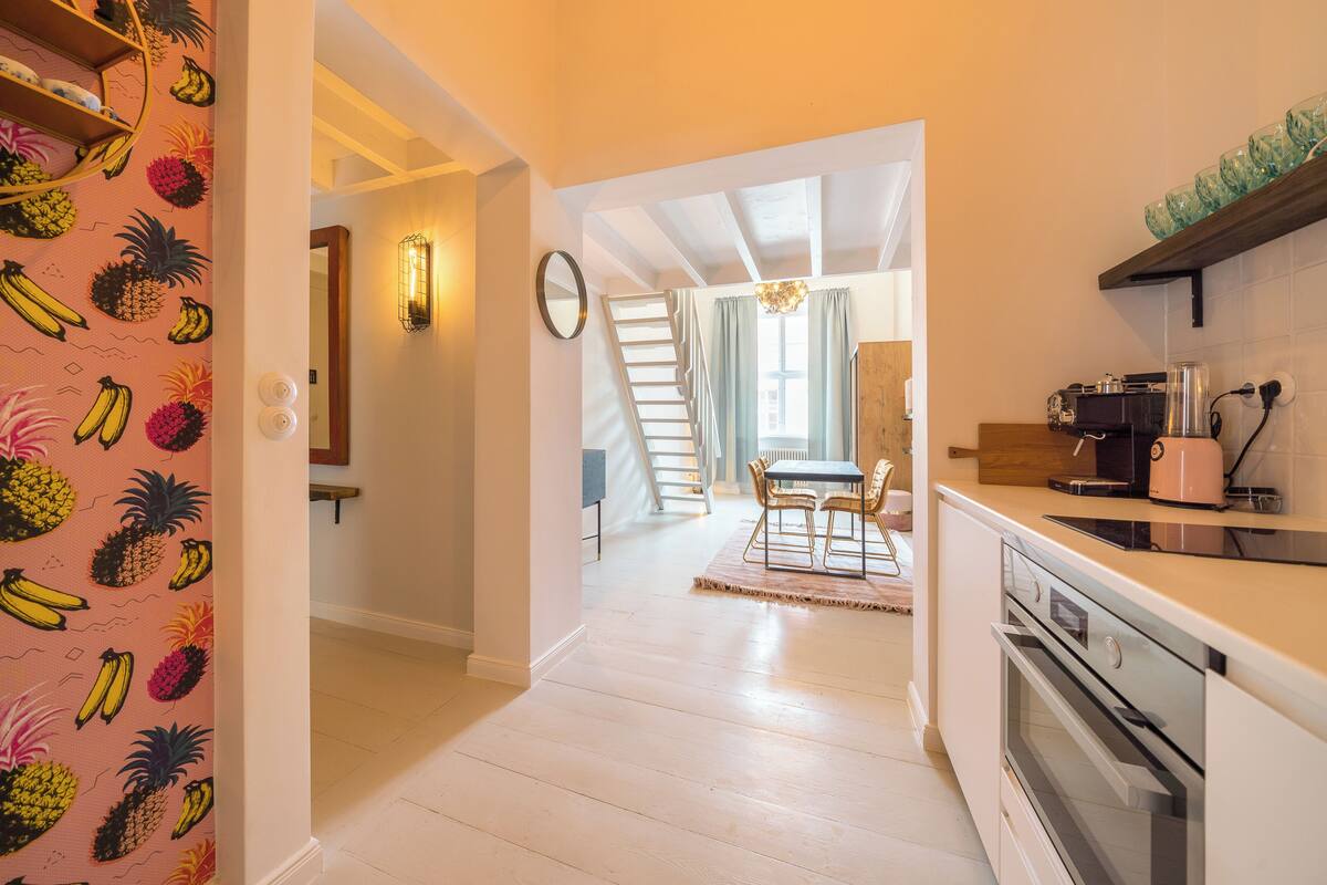 A kitchen with a wooden floor, a dining area with a table and chairs, and a staircase leading to another room.