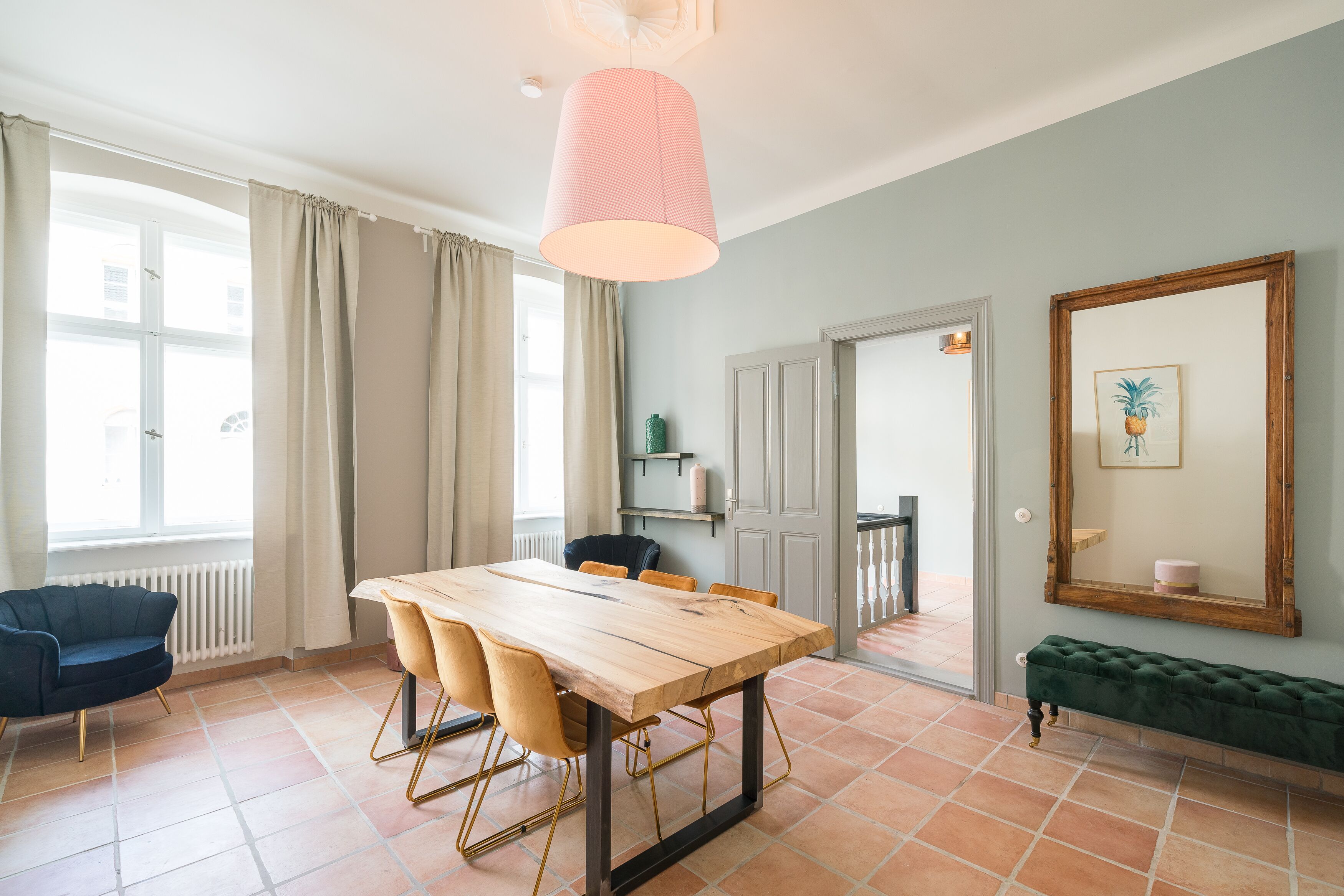 A dining area with a wooden table and chairs, a hanging light fixture, a bench, and a large mirror on the wall.