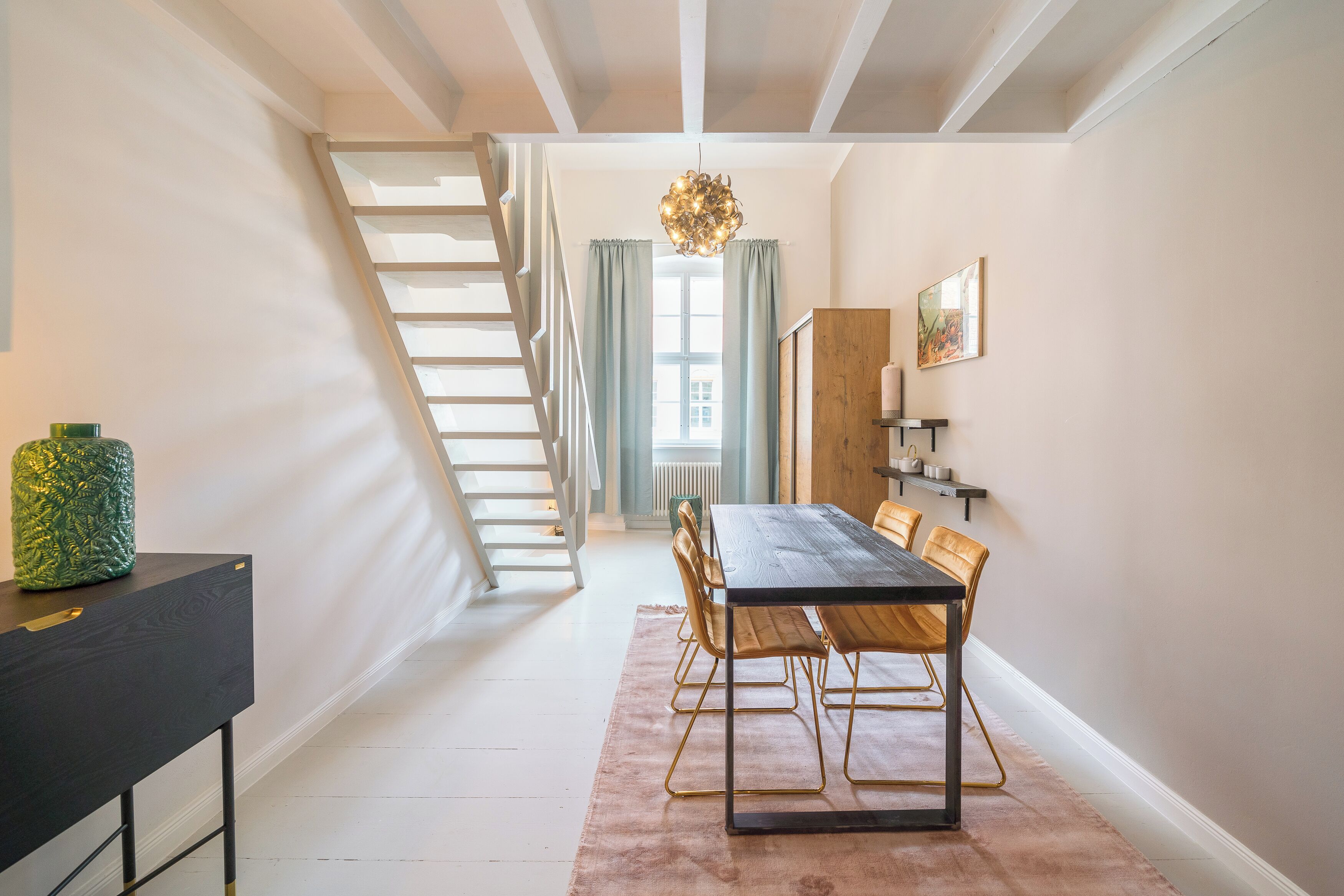 Un espace repas avec une table et des chaises en bois, un escalier et un lustre.