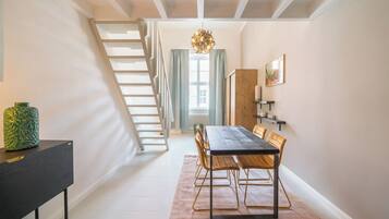Un espace repas avec une table et des chaises en bois, un escalier et un lustre.