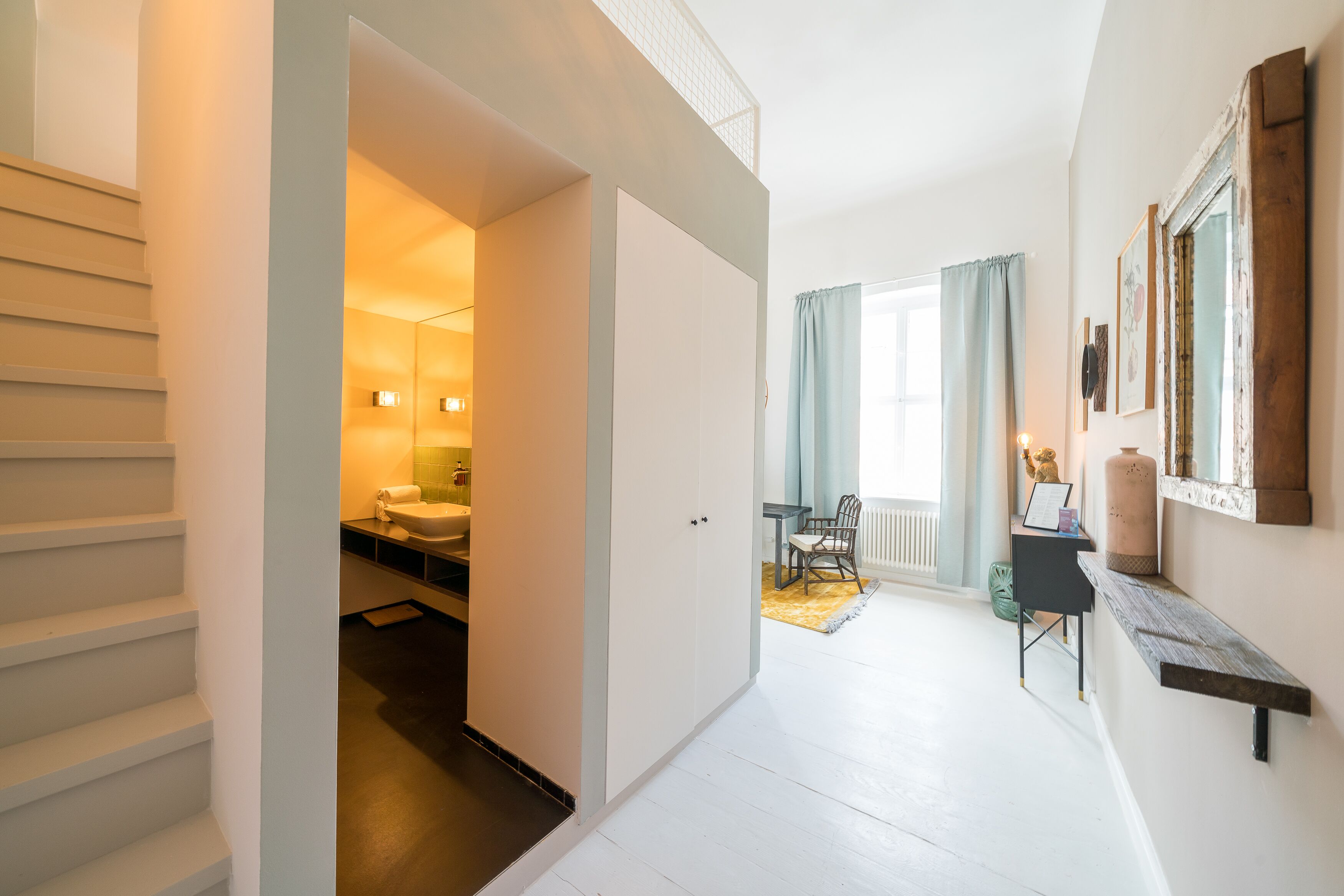 A hallway with a staircase leading to a bedroom, a dining area with a table and chairs, and a large mirror on the wall.