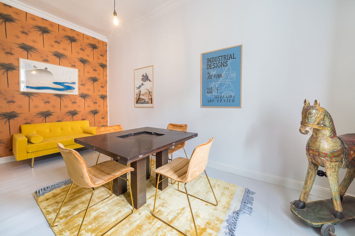 A dining area with a wooden table, four chairs, a yellow sofa, and a decorative horse sculpture.