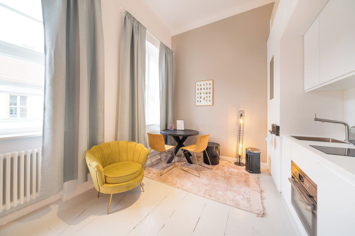 A compact living space with a yellow armchair, a round table, and a small kitchen area.