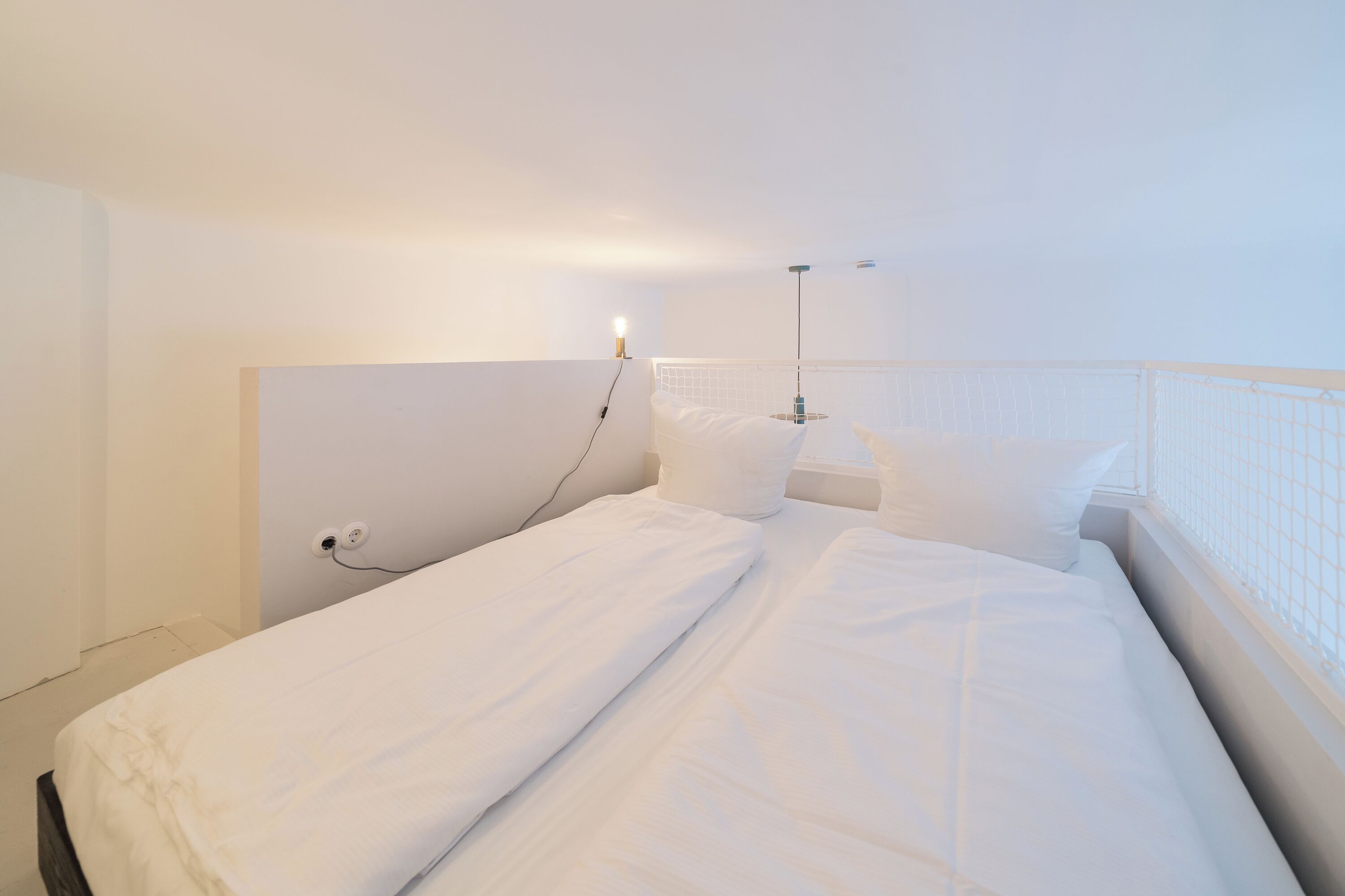 A single bed with white bedding in a room with white walls and a white headboard.