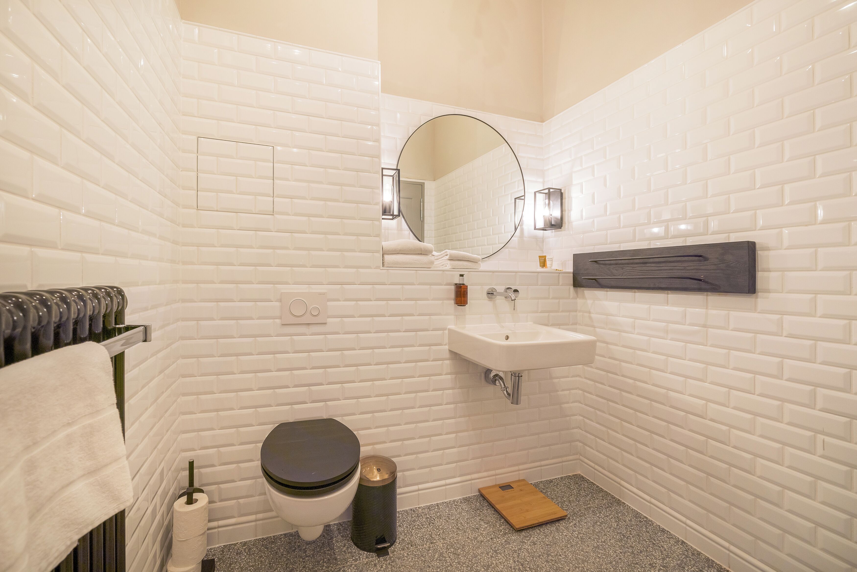 Un baño con paredes de azulejos blancos, un inodoro, un lavabo, un espejo y un perchero para toallas.