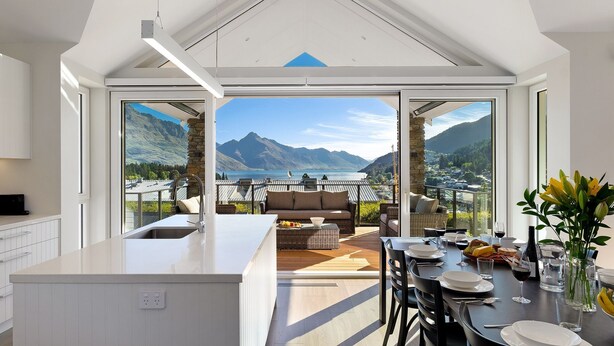 Een moderne keuken met een groot eiland, een eethoek met een tafel voor vier personen, en uitzicht op bergen en een meer.