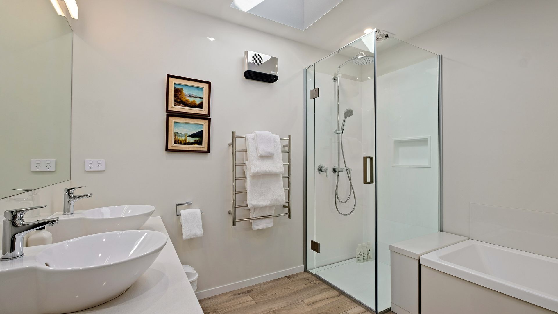 A modern bathroom with two sinks, a glass shower enclosure, and a towel rack.