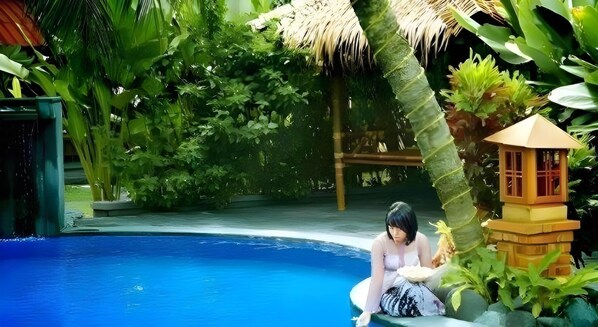 A pool surrounded by lush greenery, a thatched roof structure, and a small wooden pavilion. - Nyiur Resort Hotel (Pangandaran)