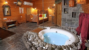 Un dormitorio tipo cabaña de madera con piso de baldosas de piedra, una cama de madera, un jacuzzi de piedra y una chimenea de piedra.