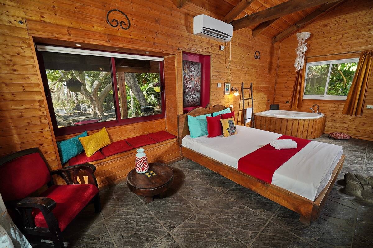 A wooden cabin room with a bed, a sofa, a small table, a window, and a bathroom.
