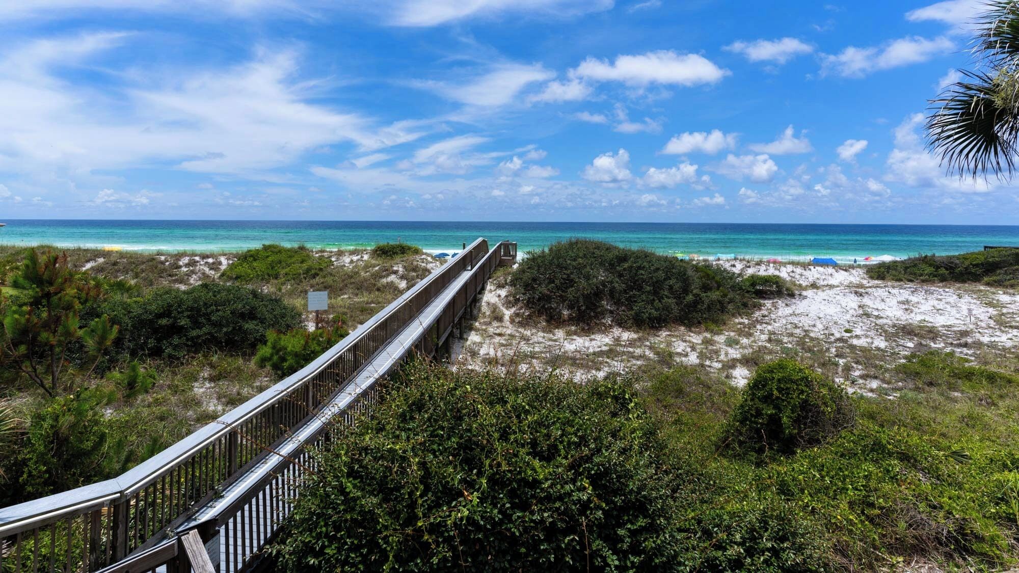 A wooden boardwalk leading to a beach with clear turquoise waters and a clear sky.