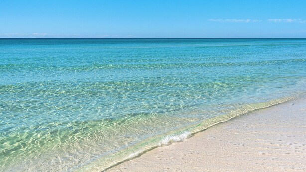 Une plage à l’eau turquoise et limpide, bordée d’un rivage sablonneux.