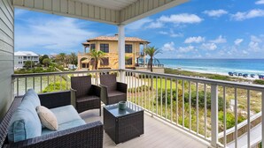 Un balcon agrémenté de meubles en osier, d’une table en verre et offrant une vue sur la plage et l’océan.