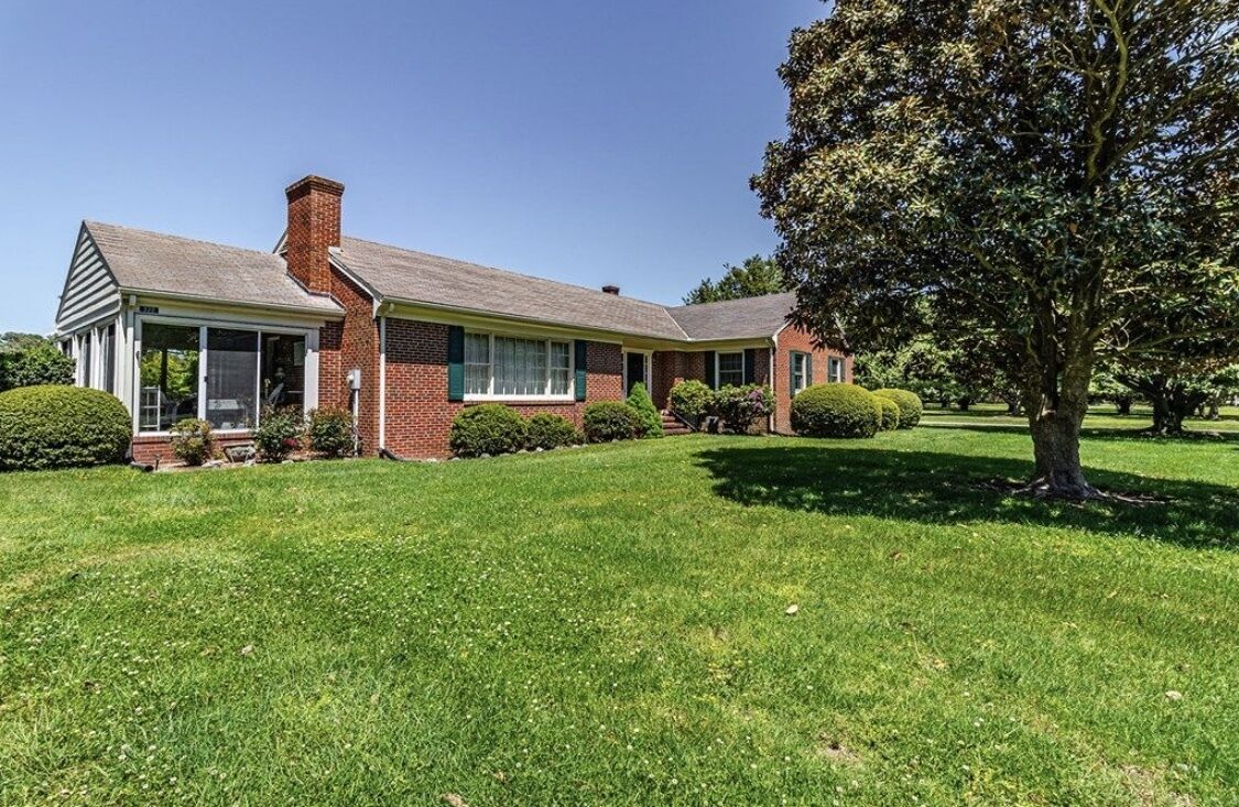 A two-story brick house with a covered porch, a well-maintained lawn, and a large tree in the front yard.