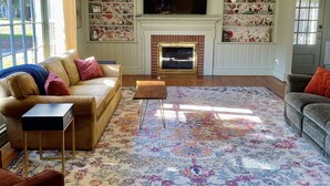 A living room with a fireplace, a television mounted above it, and a large window. - Secluded, Waterfront Retreat: Fire pit, Private Dock, Game Room, Kayaks! (Reedville)