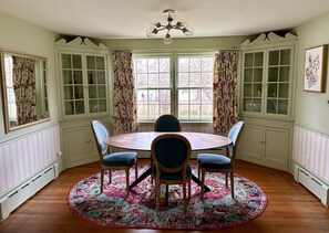 Een eetkamer met een ronde tafel, blauwe stoelen, een vloerkleed met bloemendessin en een kroonluchter.