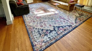 A spacious living room with a large floral rug, two sofas, a coffee table, and a window with curtains. - Secluded, Waterfront Retreat: Fire pit, Private Dock, Game Room, Kayaks! (Reedville)