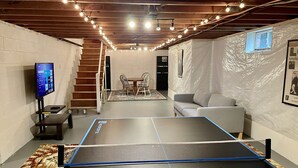 A ping pong table in a room with a wooden ceiling, a TV on a stand, and a couch. - Secluded, Waterfront Retreat: Fire pit, Private Dock, Game Room, Kayaks! (Reedville)