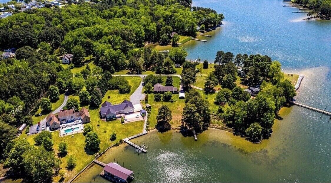 An aerial view of a lakeside property with multiple houses, a dock, and a swimming pool.
