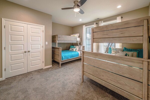 A room with a bunk bed, a dresser with glass drawers, a ceiling fan, and a door.