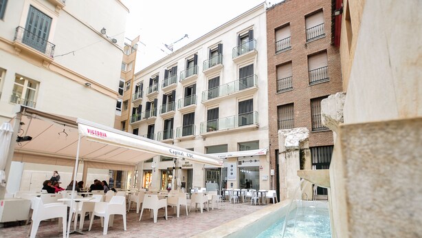 Ein Straßencafé mit weißen Stühlen und Tischen, einem Pool und Gebäuden im Hintergrund.