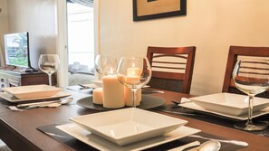 Mesa de comedor servida con platos blancos, vasos y velas, con vista al exterior.