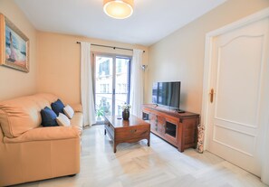Un salón con un sofá, una mesa de centro, un televisor sobre un mueble de madera y una puerta.