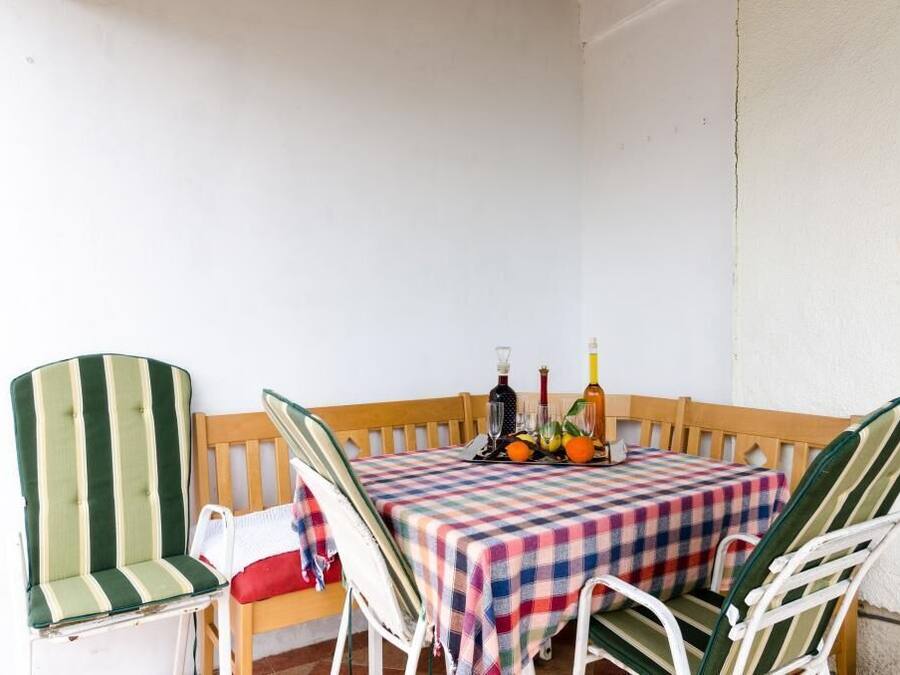Un pequeño espacio al aire libre para comer con mantel a cuadros, dos sillas a rayas y un banco de madera.