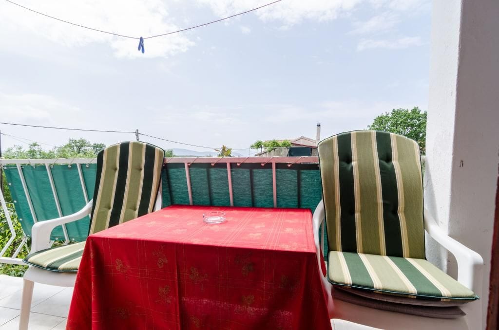 Ein Balkon mit zwei gestreiften Stühlen und einem Tisch, der mit einer roten Tischdecke bedeckt ist.