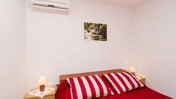 A bedroom with a single bed, a nightstand with a lamp, an air conditioner, and a wall-mounted picture.