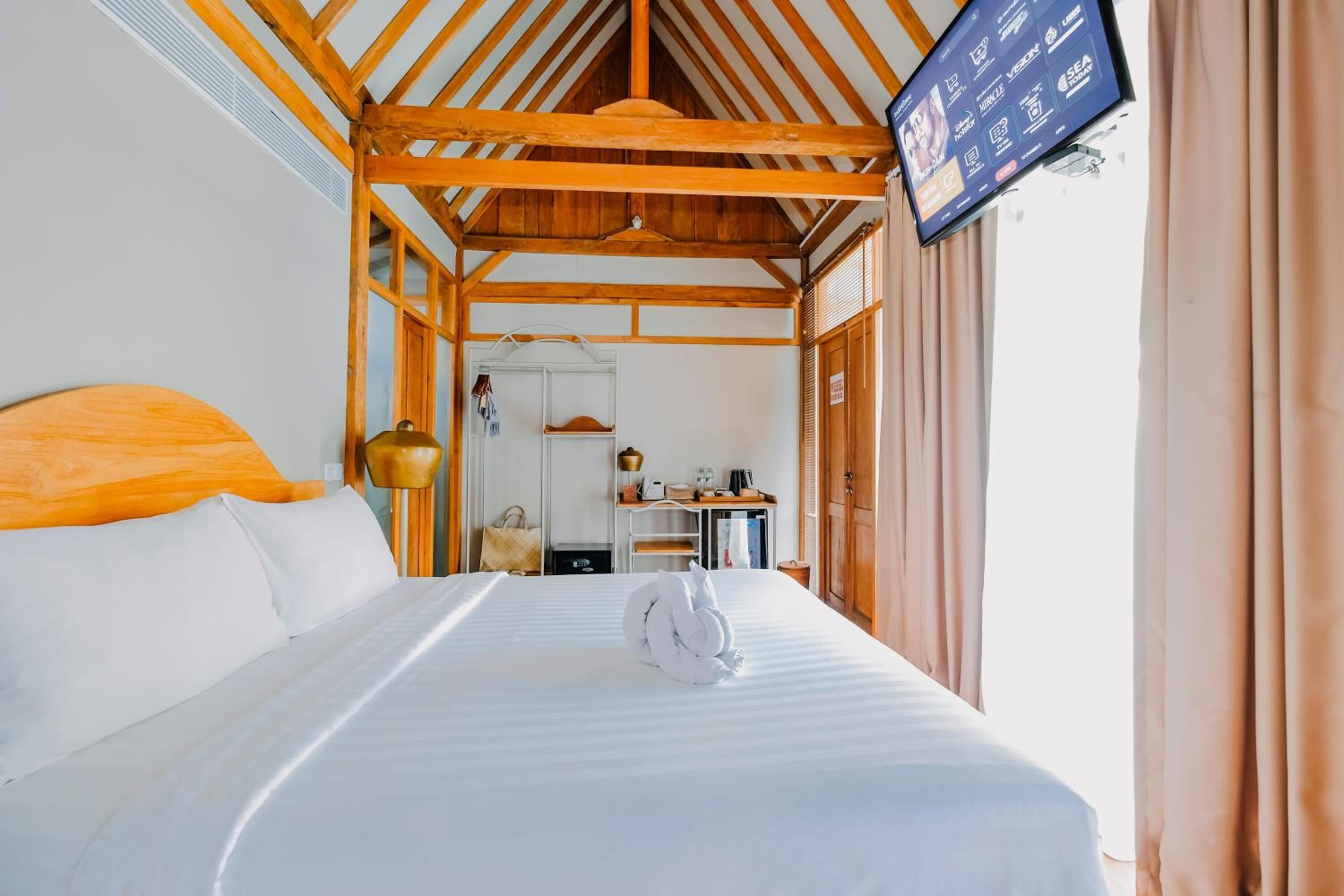 Habitación de hotel con techo de madera, cama con ropa blanca, televisor montado en la pared y vista del interior de la habitación.
