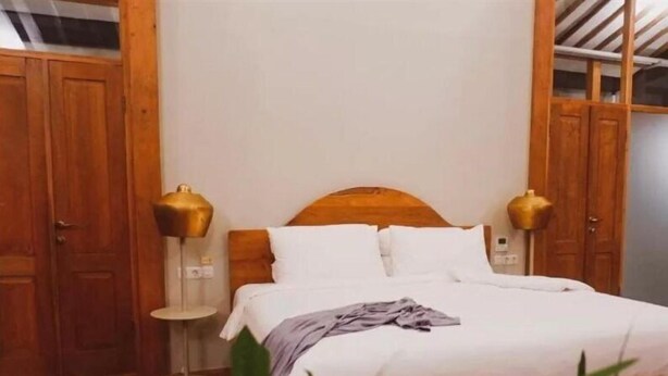 A bedroom with a wooden bed, white bedding, and two bedside lamps. - Ayom Java (Surakarta)