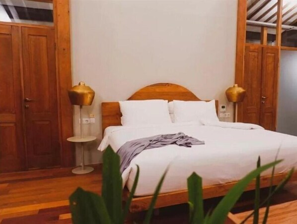 A bedroom with a wooden bed, white bedding, and two bedside lamps. - Ayom Java (Surakarta)