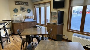 A restaurant interior with wooden tables and chairs, a 'Welcome' sign, decorative wall art, a TV, and a window view. - The Center Inn (Sioux Falls)
