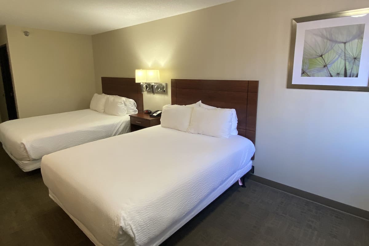 A hotel room with two beds, a nightstand with a lamp, and a framed abstract painting on the wall.