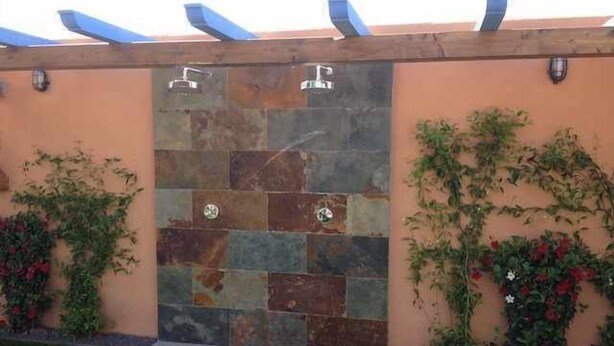 A stone wall with a built-in shower, surrounded by greenery and flowers. - House 1 suite Ragel coast (Palmar, El)