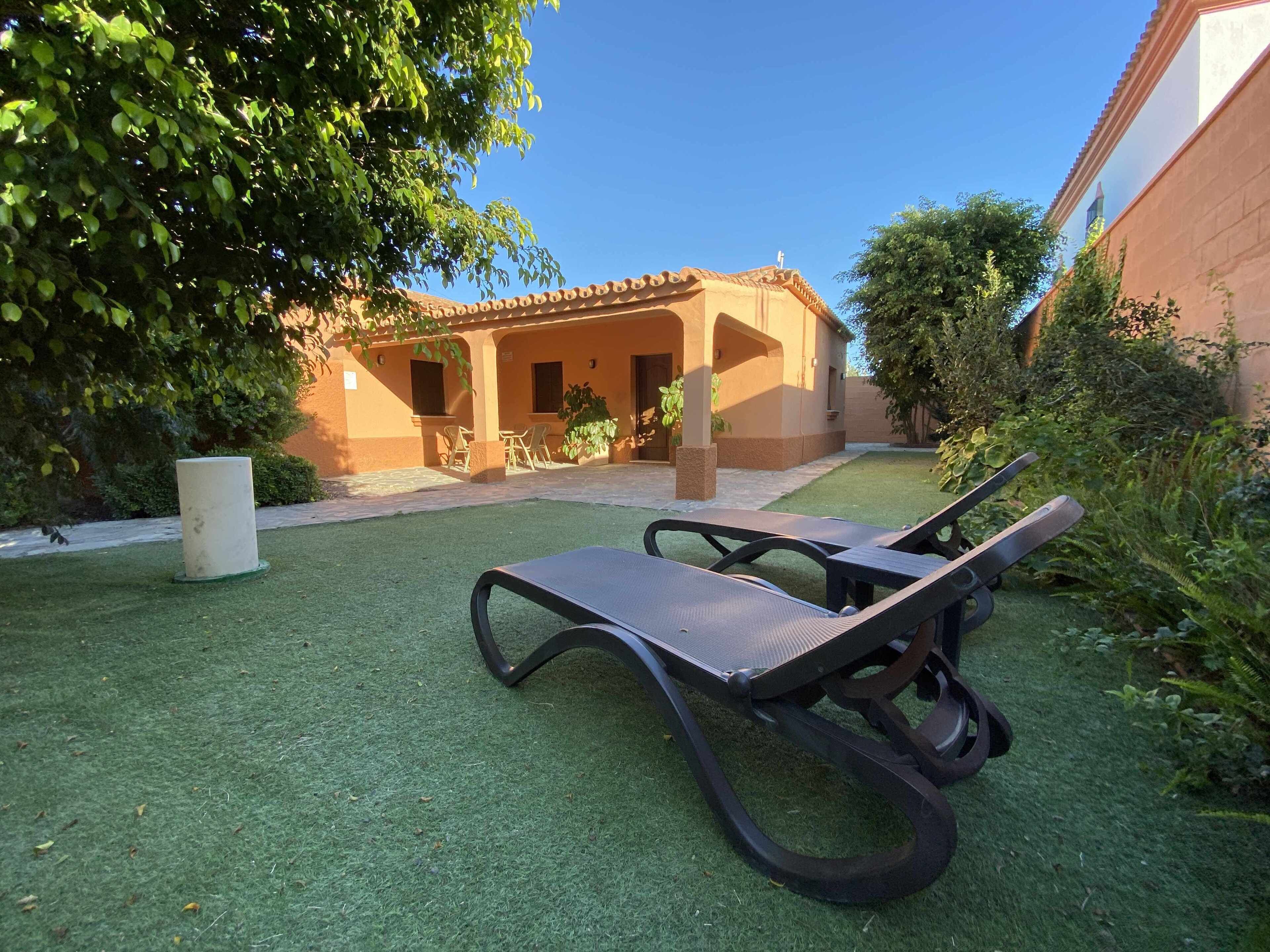 Un patio con dos sillones, una mesita y un edificio con tejado de baldosas al fondo.