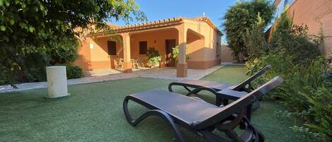 Un patio con dos sillones, una mesita y un edificio con tejado de baldosas al fondo.